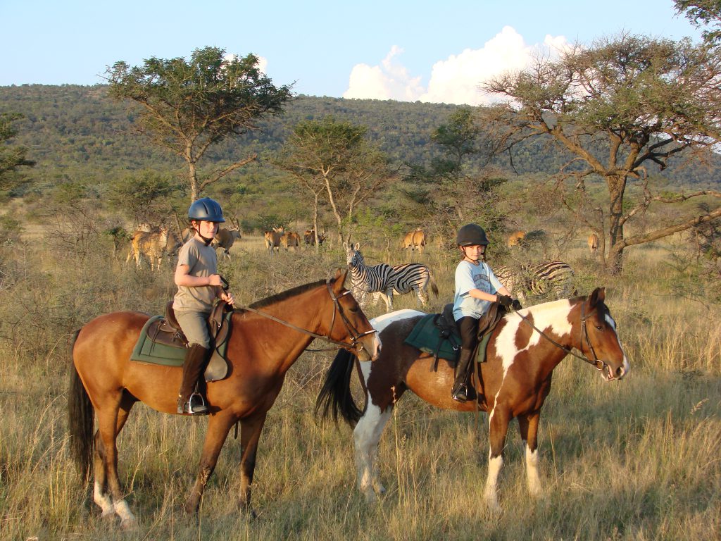 Twee kinderen op een paard met zebra's op de achtergrond tijdens een safari