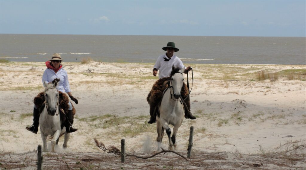 Twee ruiters en paarden rijden door de duinen in Brazilië met de zee op de achtergrond