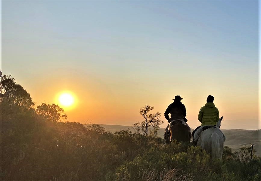 Twee ruiters en paarden kijken uit over de bergen van Brazilië bij zonsondergang
