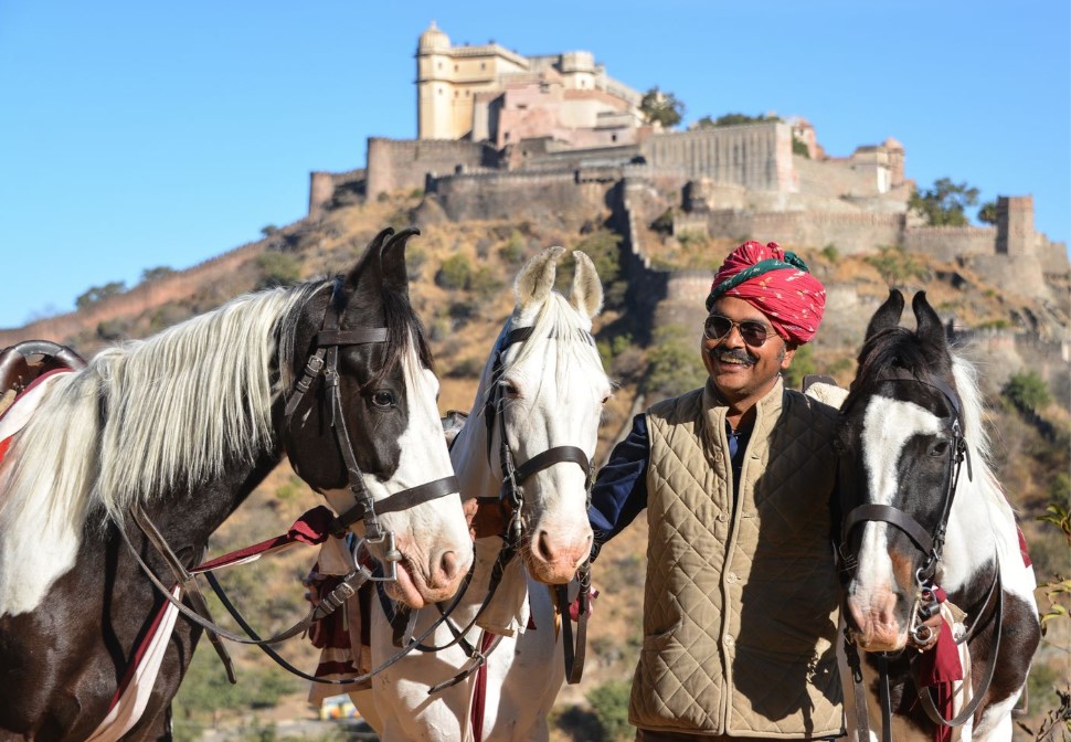 Gids met drie paarden en een kasteel op de achtergrond tijdens een paardrijvakantie in India.