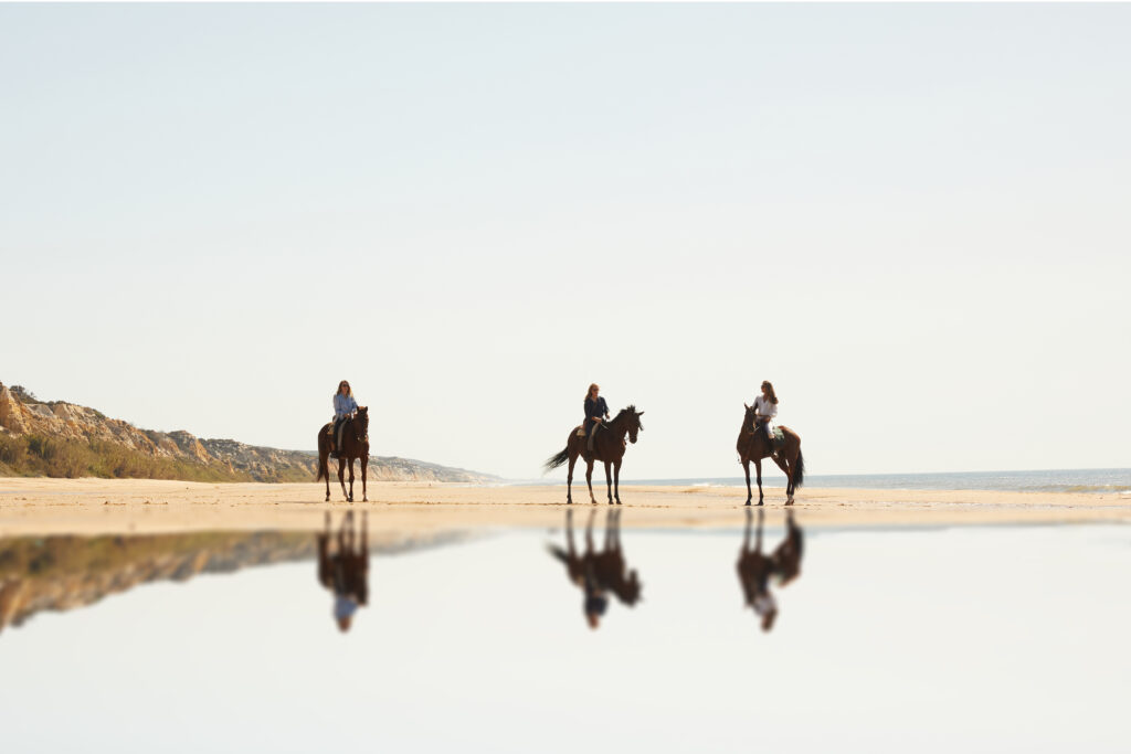 Drie ruiters en paarden op het strand van Spanje tijdens een buitenrit.