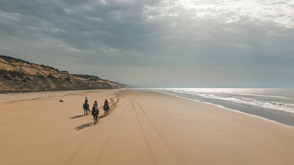 Drie ruiters en paarden op het strand van Spanje tijdens een buitenrit.