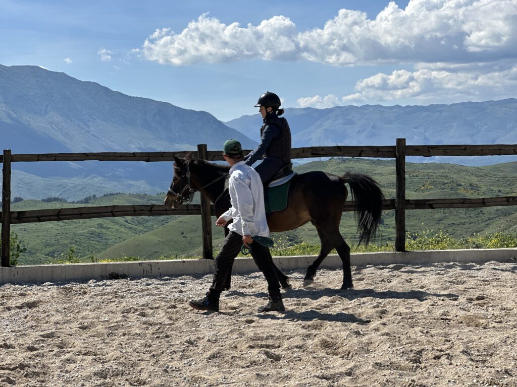 Ruiter en paard met een instructeur ernaast in de bak tijdens een paardrijvakantie in Albanië, op de achtergrond zie je bergen.