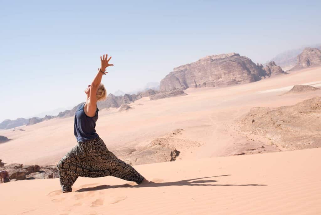 Vrouw doet een yoga pose op een zandduin in de woestijn van Jordanië