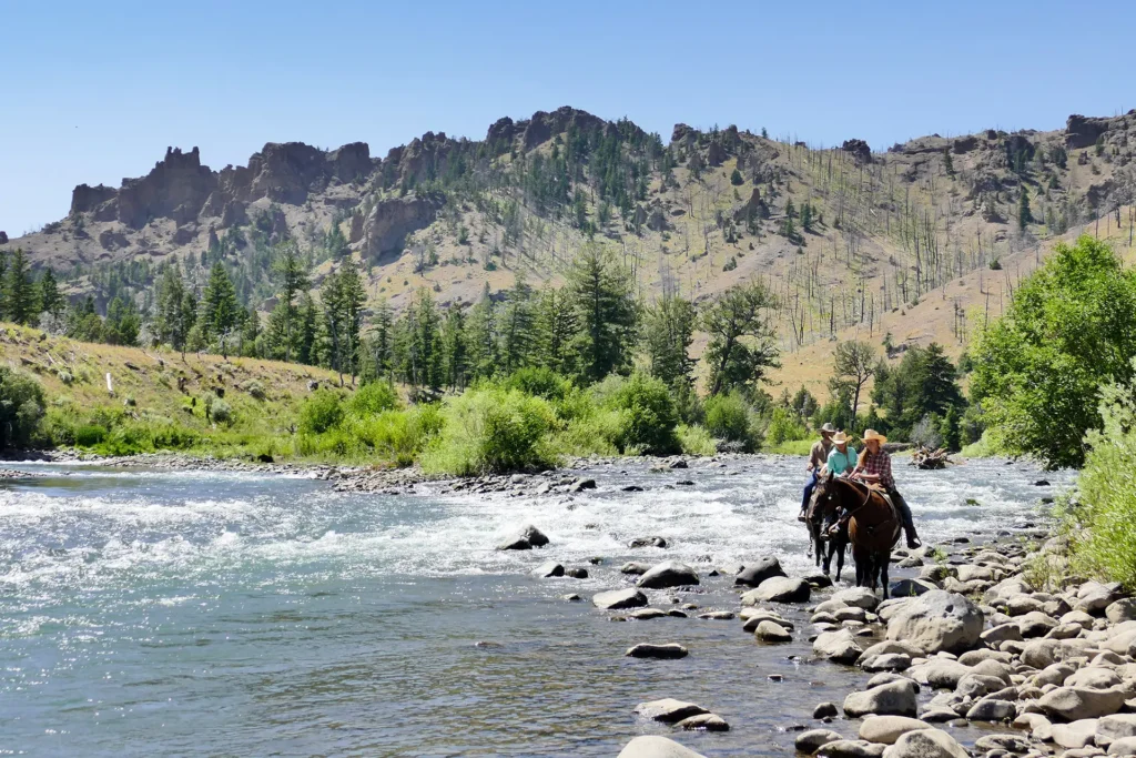 Ruiters en paarden rijden door een rivier met bergen op de achtergrond in de buurt van Yellowstone in Wyoming