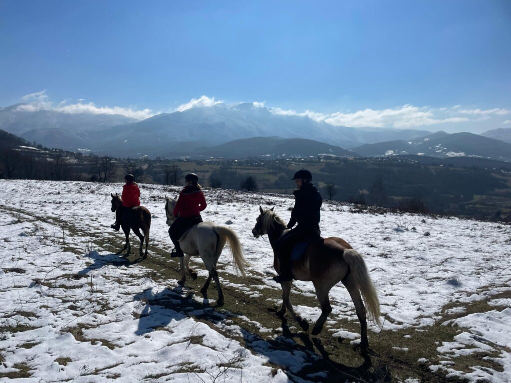 Groepje ruiters en paarden in de sneeuw met bergen op de achtergrond in Bosnië